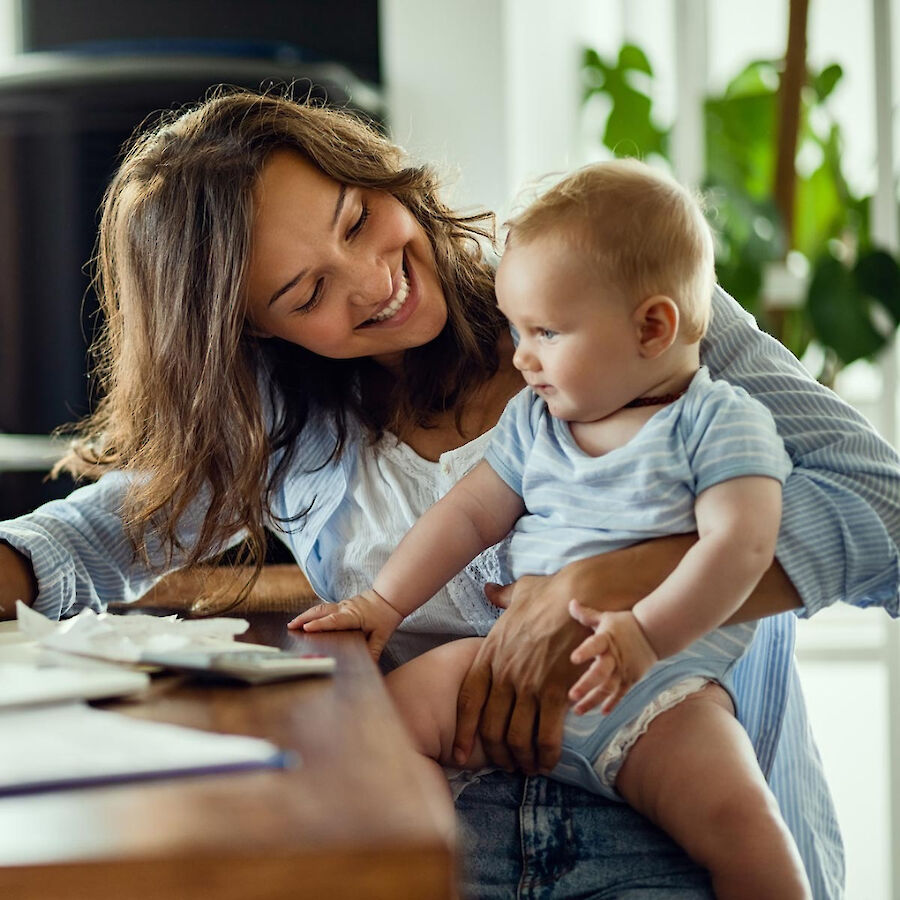 Lächelnde Mutter hält ihr Baby auf dem Schoß und schaut es liebevoll an.