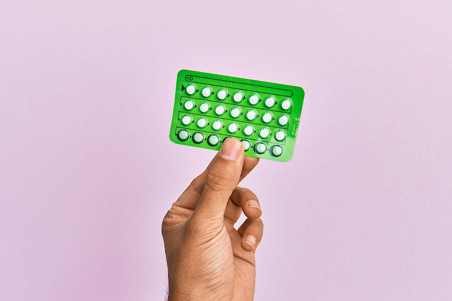 Hand hält eine grüne Pillenpackung zur hormonellen Empfängnisverhütung.“