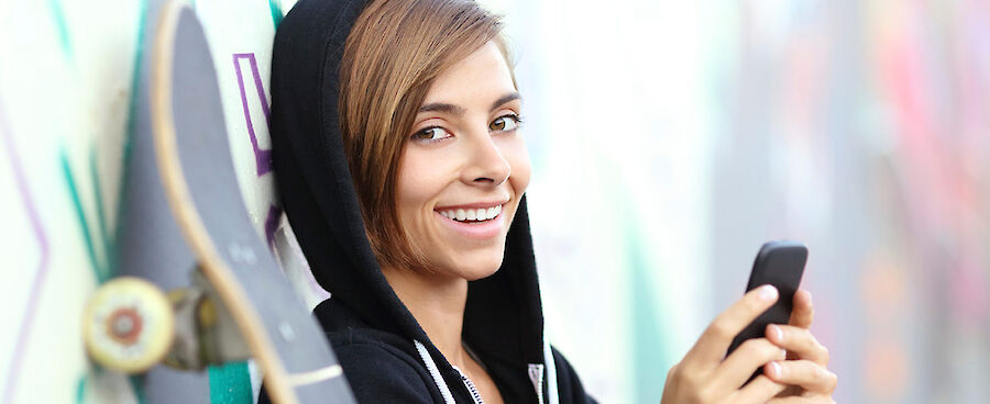 unge Frau mit Skateboard und Smartphone vor einer Graffiti-Wand.“