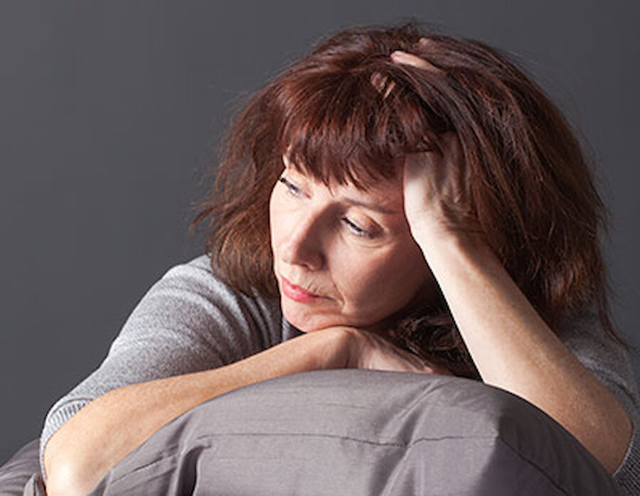 Nachdenkliche, depressieve Frau sitzt mit gesenktem Blick und stützt den Kopf auf ihre Hand.